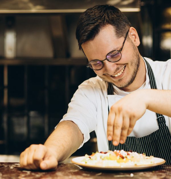 Man chef at the kitchen sprinkles sald from cabbage with pomegranate